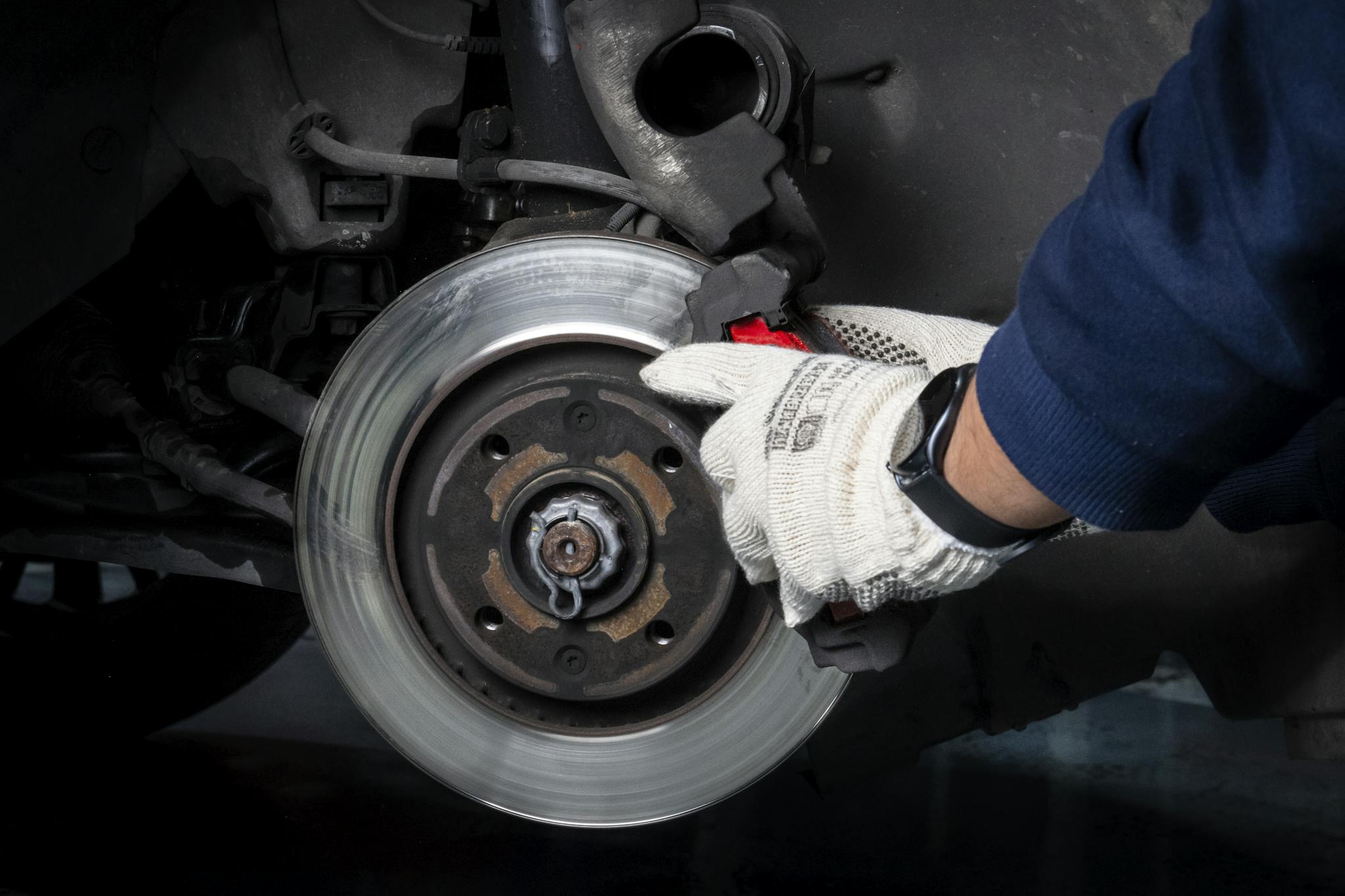 Mechanic working on car brake system in a workshop setting.